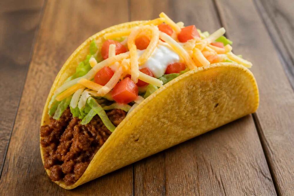 Taco z mielonym mięsem, sałatą, pomidorem, serem i kwaśną śmietaną na drewnianym stole